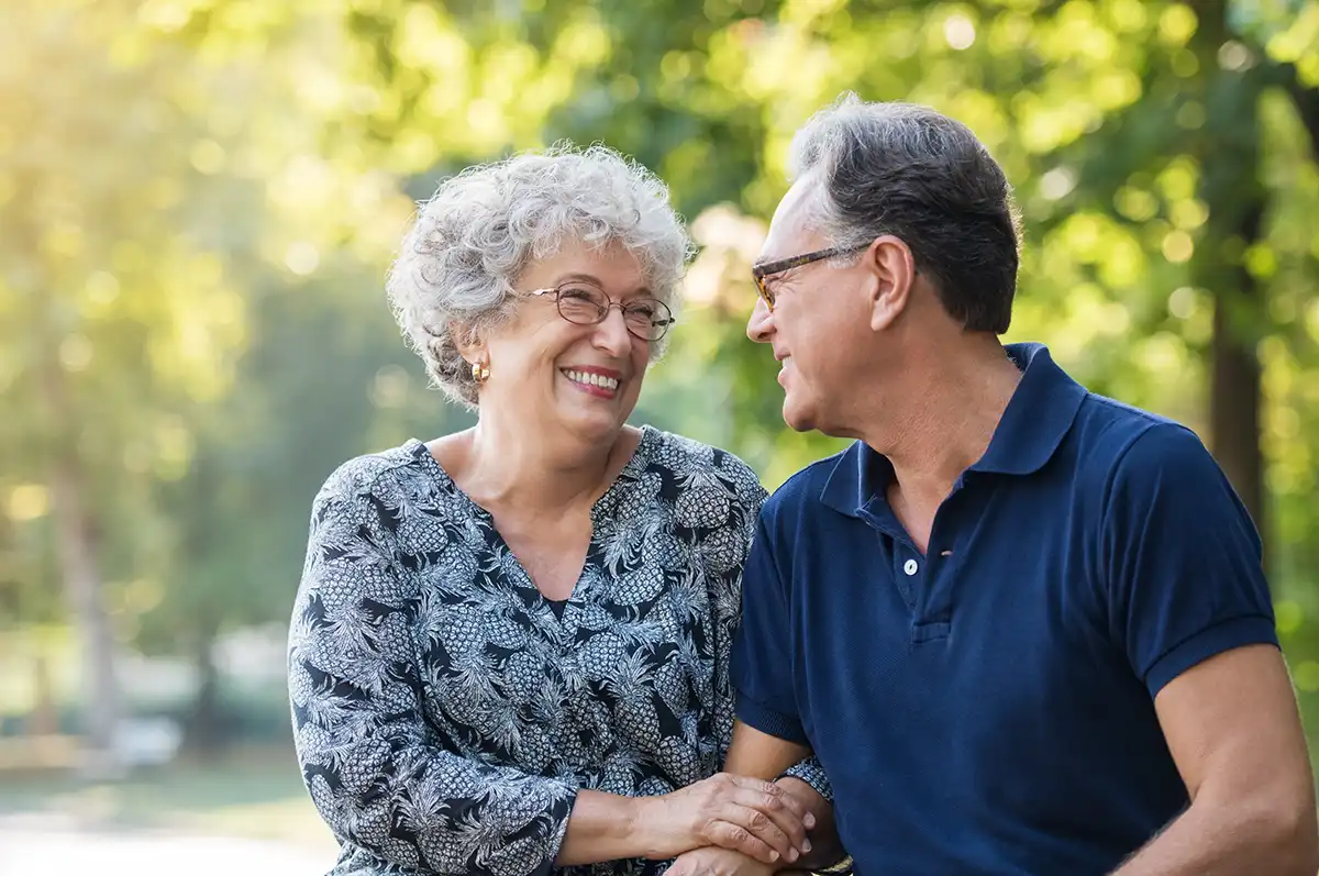 A senior couple look at each other with locked arms while outdoors