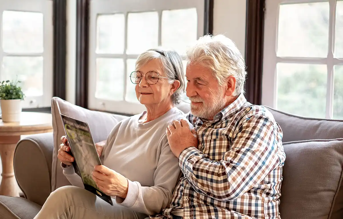 A senior couple sit on a couch and read a magazine together