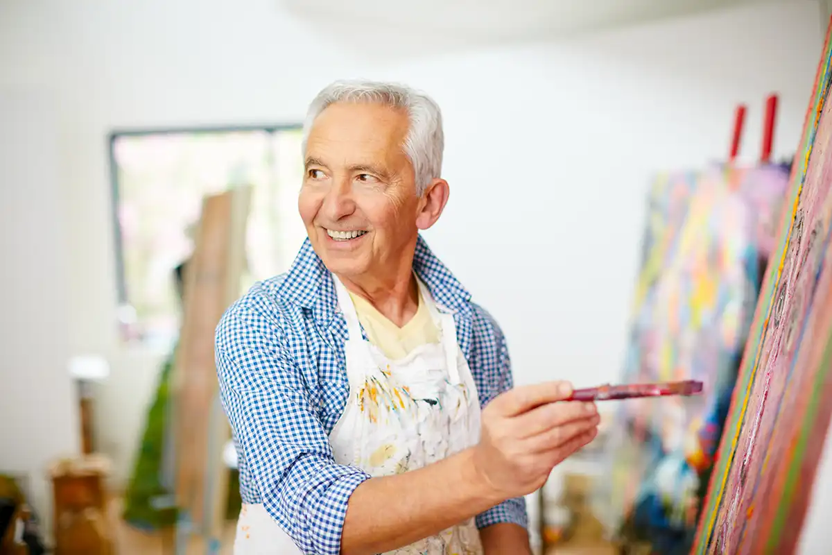 a senior man stand at an easel with a fine-art paintbrush