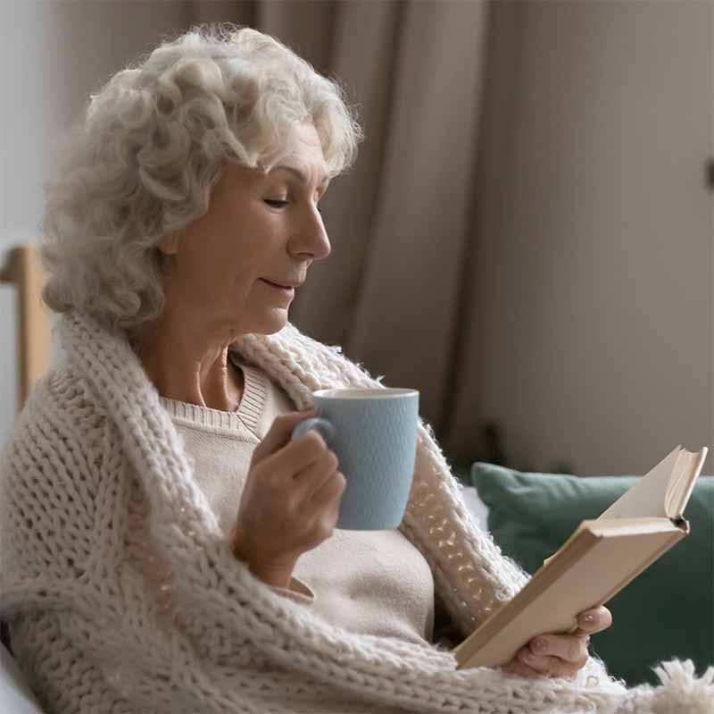 Woman warm and cozy inside with hot chocolate and a book